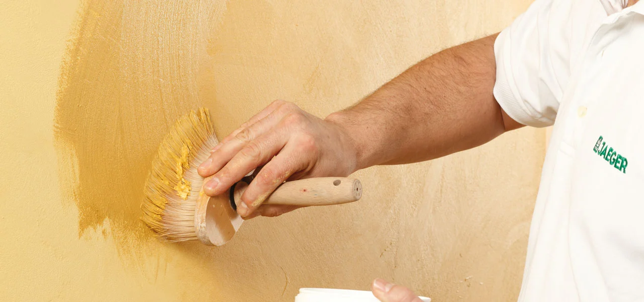 Mit einem Pinsel wird Antikseife an der Kalkputzwand aufgebracht.