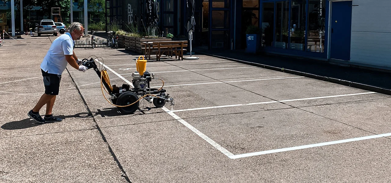 Person, die mit einem Markiergerät Parkplätze markiert, symbolisch für die Markierworkshops